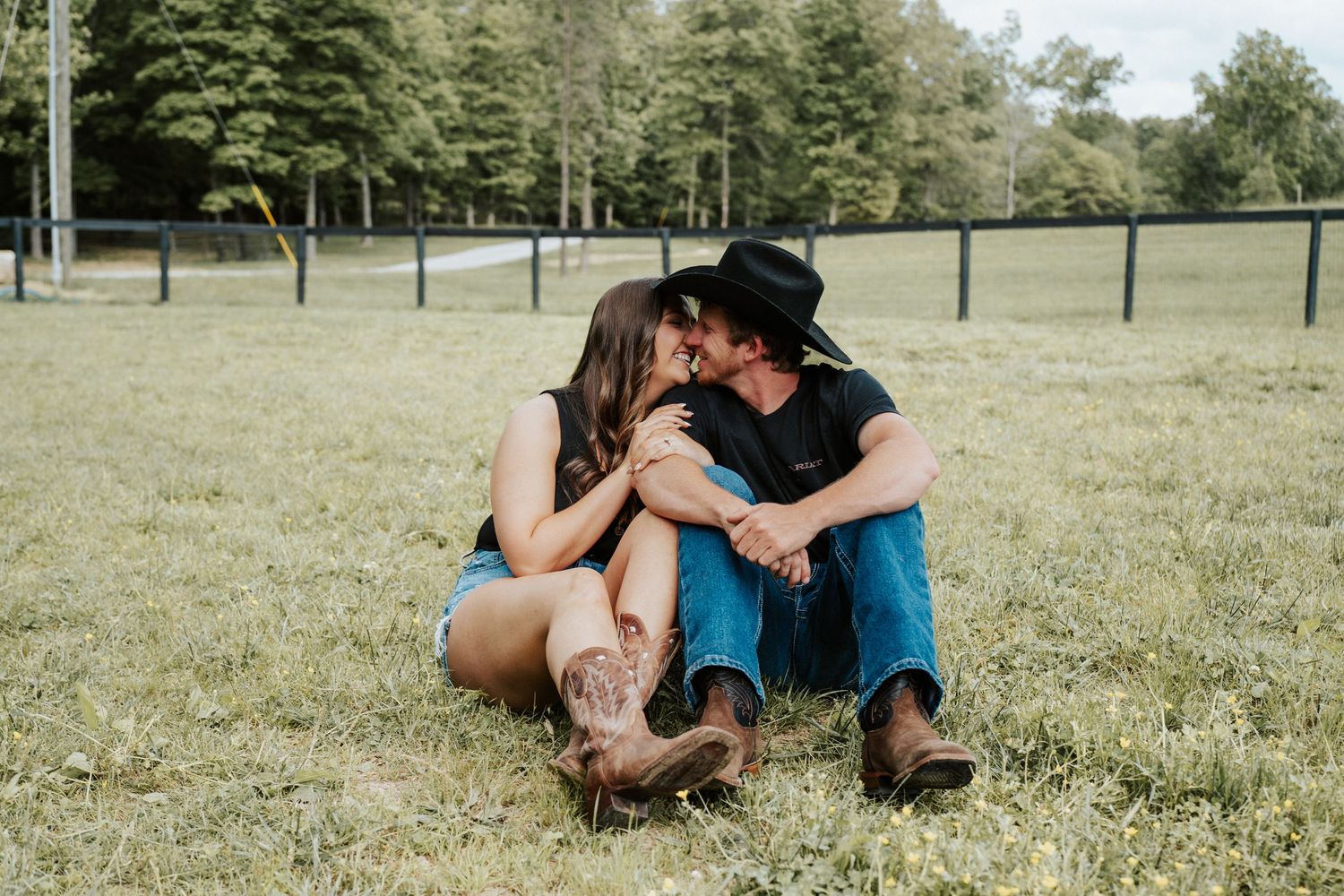 Couple in cowboy boots sitting together on grass in a sunny field.