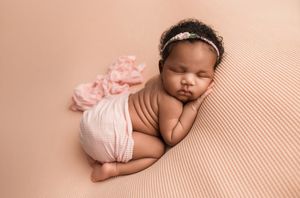 Sleeping newborn wearing white wrap on blush pink backdrop with delicate floral decorations.