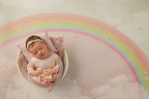 A rainbow appears behind a sleeping newborn baby wrapped in pink blanket during a professional photoshoot.