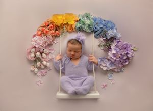 Sleeping newborn in purple outfit on swing under rainbow of flowers in composite collection of images.