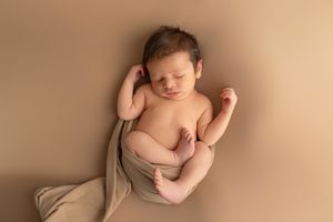 Sleeping newborn baby wrapped in soft beige fabric on warm neutral background during professional photoshoot.