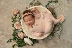 A newborn baby rests peacefully on a pink blanket surrounded by delicate floral decorations and greenery.