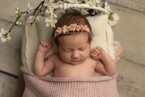 Sleeping newborn in pink knit wrap with floral headband and white flowers in background.