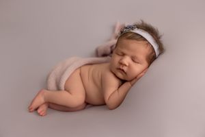 A sleeping newborn baby lies peacefully on soft pink fabric in a professional studio photography setting.