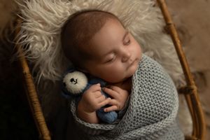 A sleeping baby wrapped in soft gray knitted blankets in a rustic wooden basket.