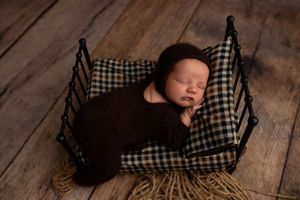 Baby in checkered black and white outfit lying on rustic wooden floor wrapped up in dark blanket for newborn photoshoot.