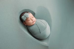 Sleeping newborn wrapped in soft sage green swaddle photographed in heart-shaped setting with matching headband.