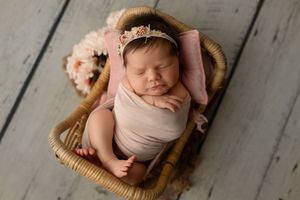 A series of newborn photography shots showing a sleeping baby wrapped in pink fabric on wooden floors and in baskets.