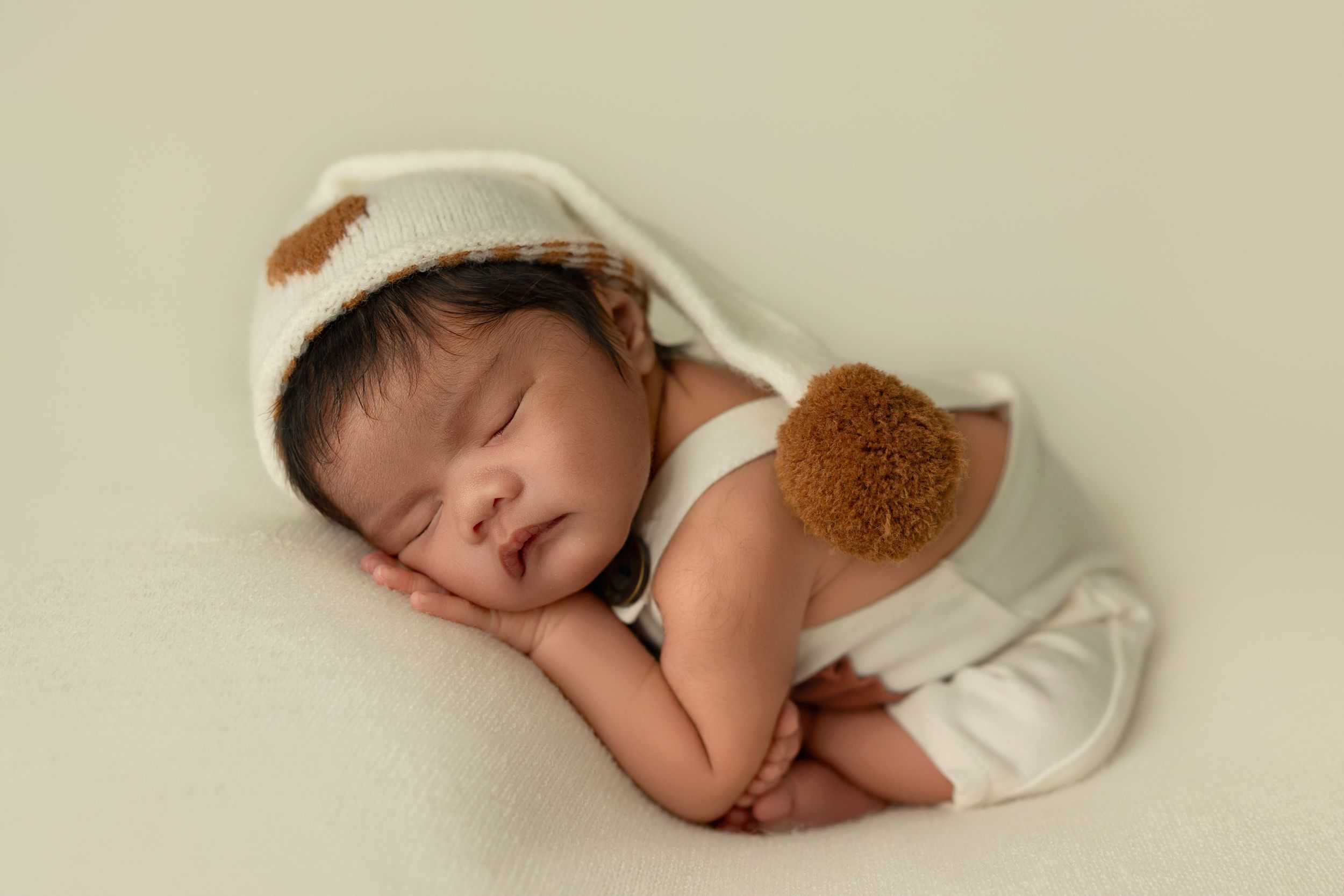 A sleeping baby wrapped in a white blanket lies peacefully against a beige background.