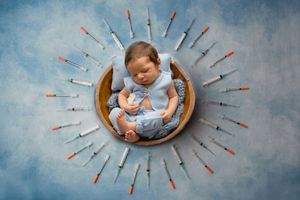 A sleeping baby nestled in a round wooden bowl surrounded by colorful arrows arranged in a sunburst pattern on blue background.
