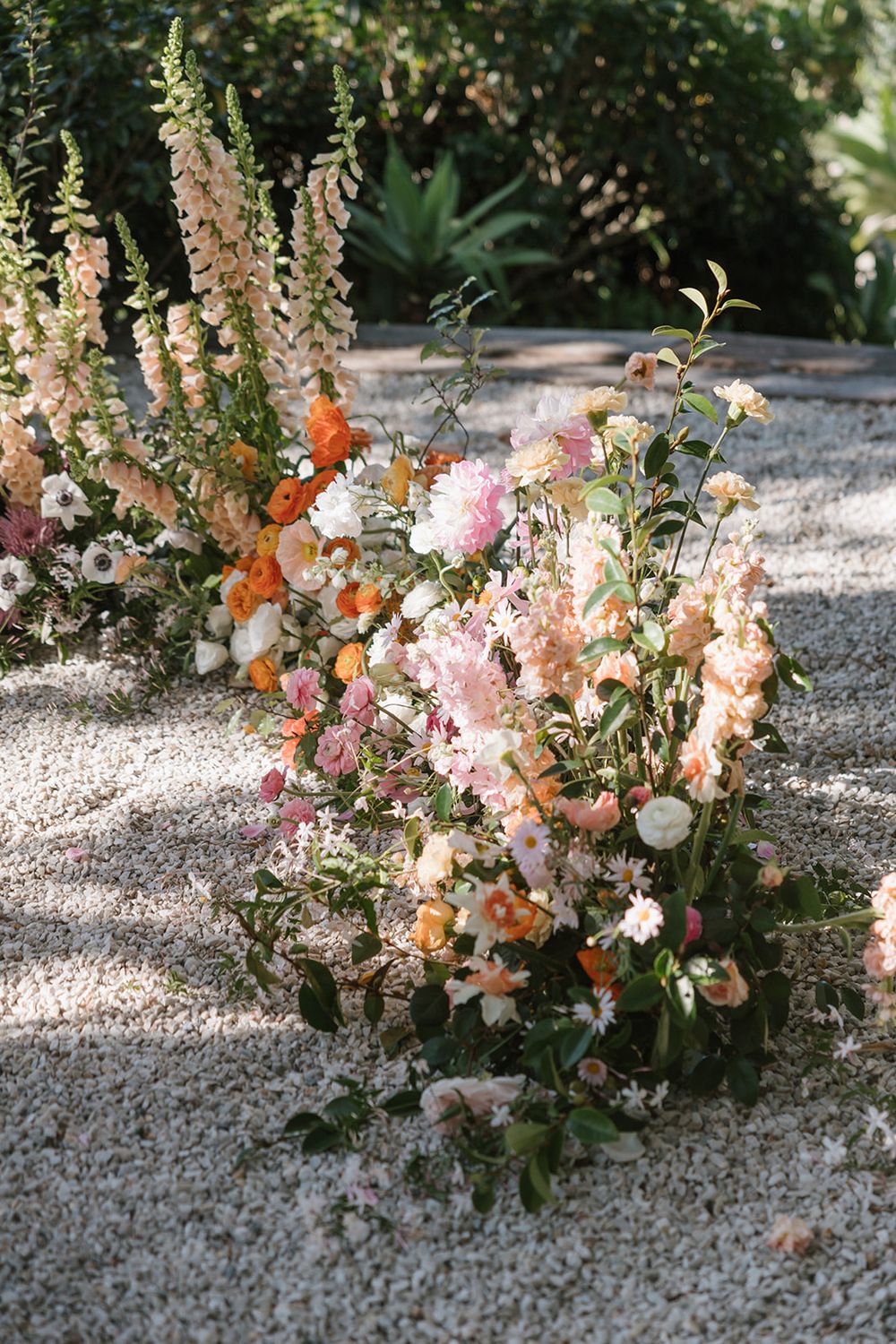 Romantic garden floral arrangement featuring peach and pink snapdragons with mixed blooms on gravel path.