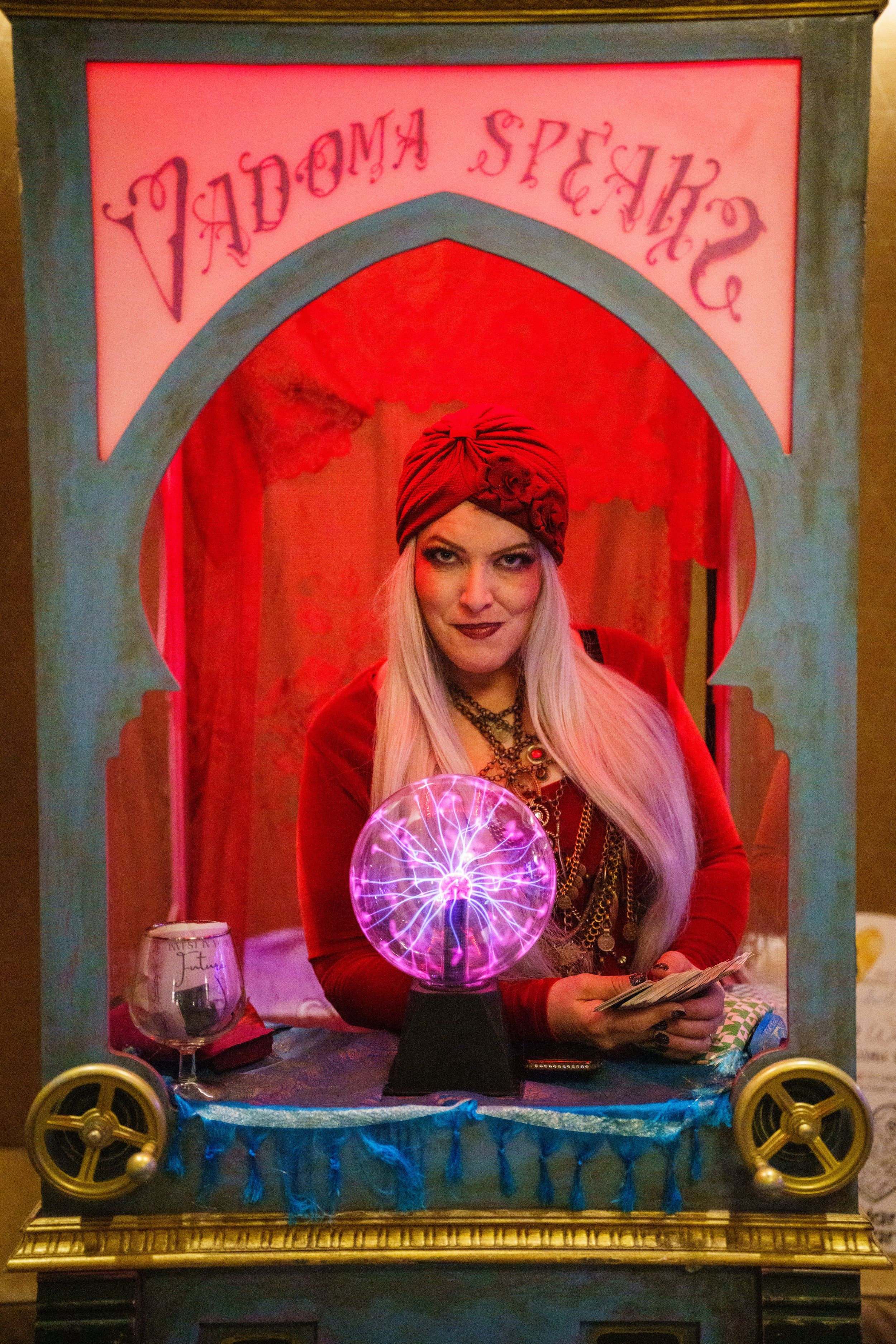 A fortune teller booth with a glowing purple plasma ball and ornate gold frame illuminated in dramatic red lighting.