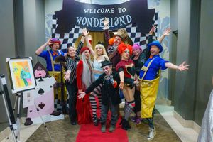 A costumed group poses under a Welcome to Wonderland sign at a themed event with playing card decorations.