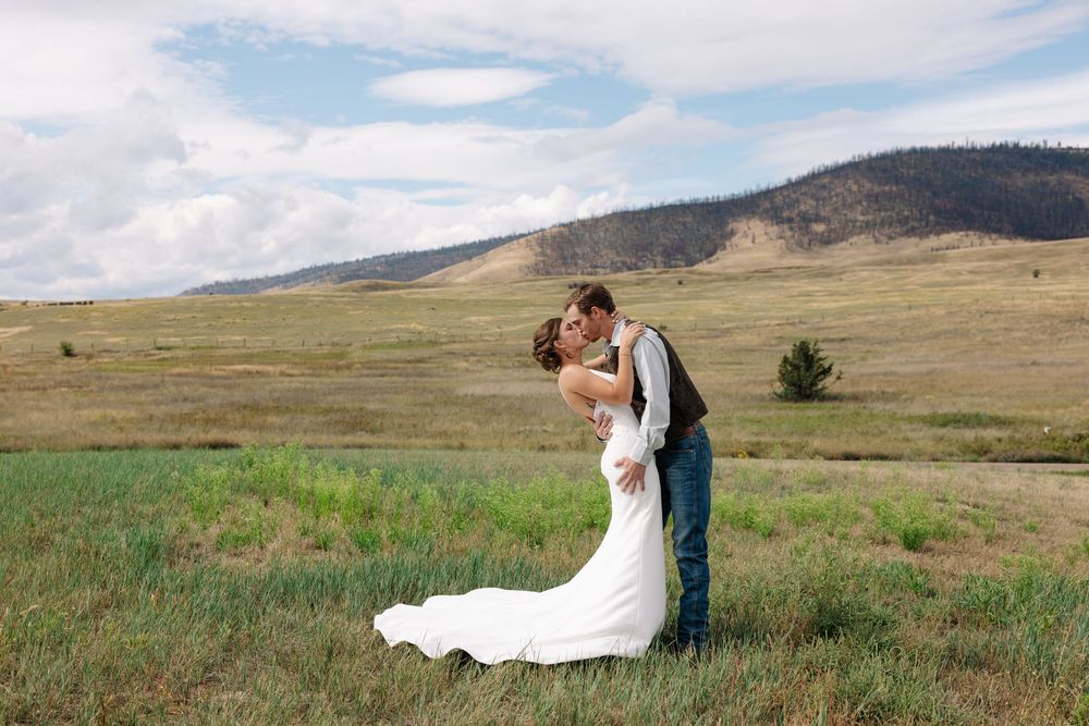 Newlyweds embrace in a scenic mountain meadow during their wedding photoshoot.