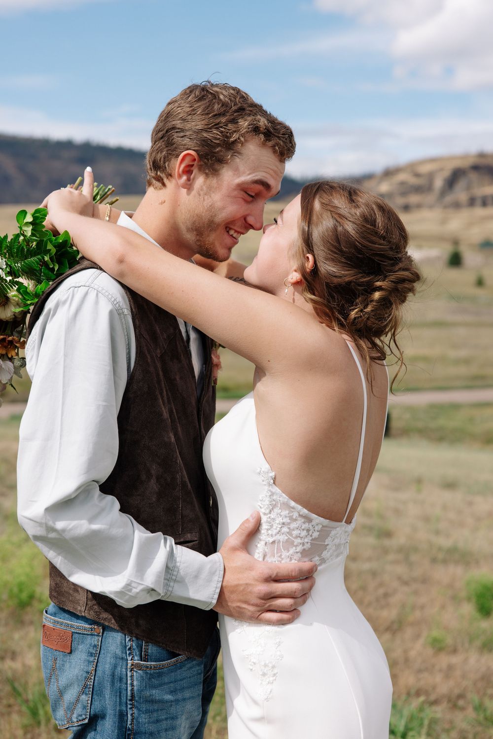 Couple embraces outdoors during rustic country wedding with rolling hills in background.