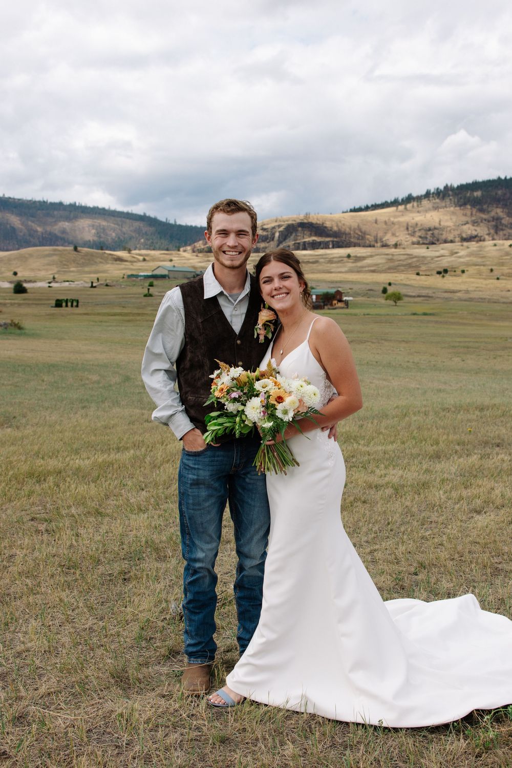 Newlyweds posing in rustic outdoor setting with bride holding floral bouquet.