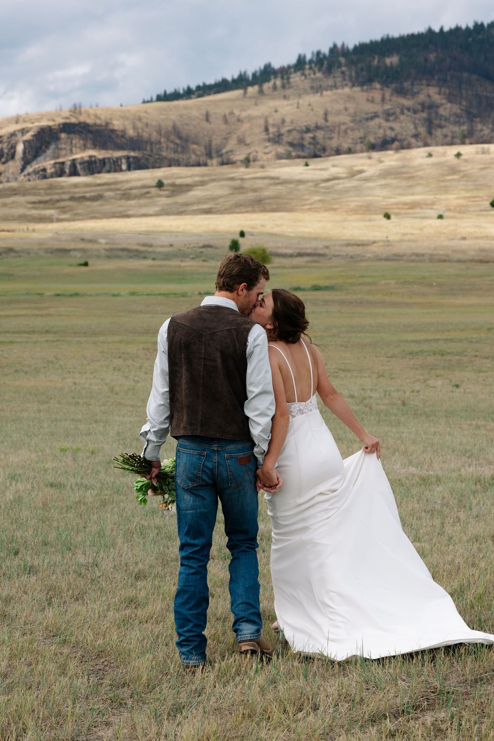 A romantic couple walking hand in hand through mountain meadow with flowing wedding dress.
