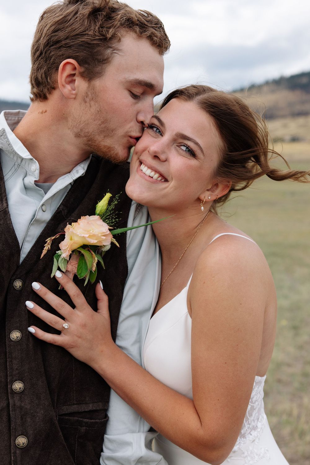 A tender wedding moment shows a couple embracing in an outdoor field with the groom wearing a boutonniere.