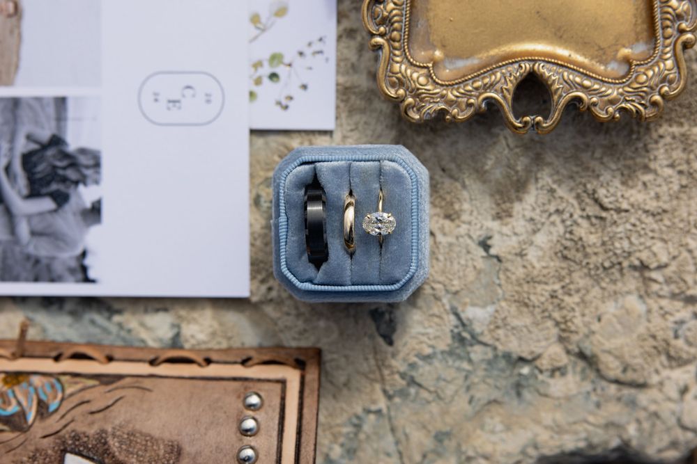 A vintage-style blue ring box with wedding rings displayed on a textured surface.