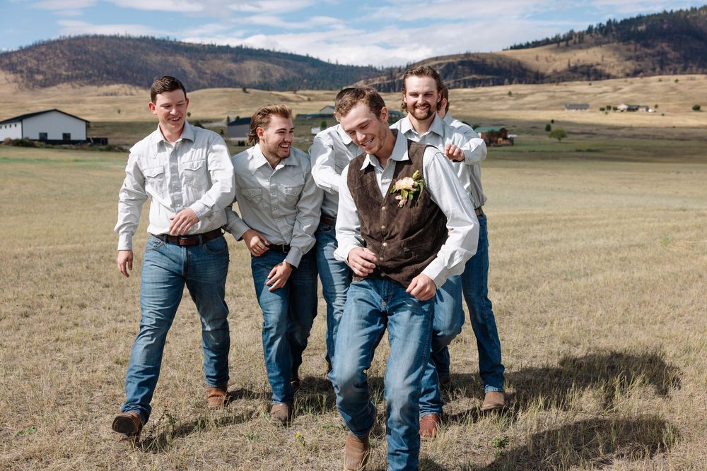 Groomsmen in western attire laughing together on a rural ranch.