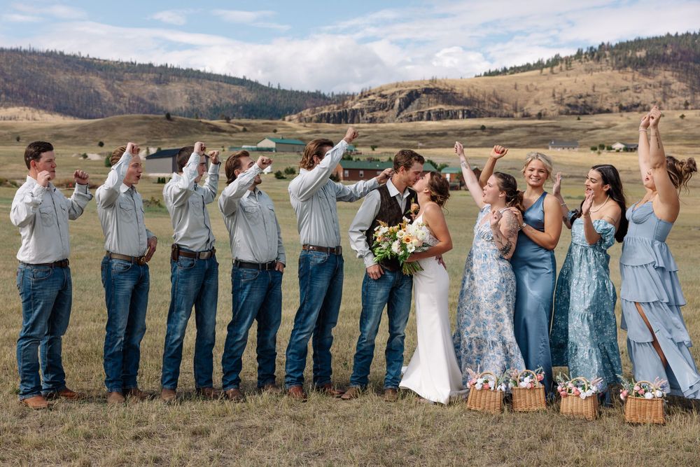 Wedding party strikes fun poses together in an open field with mountains in the background.