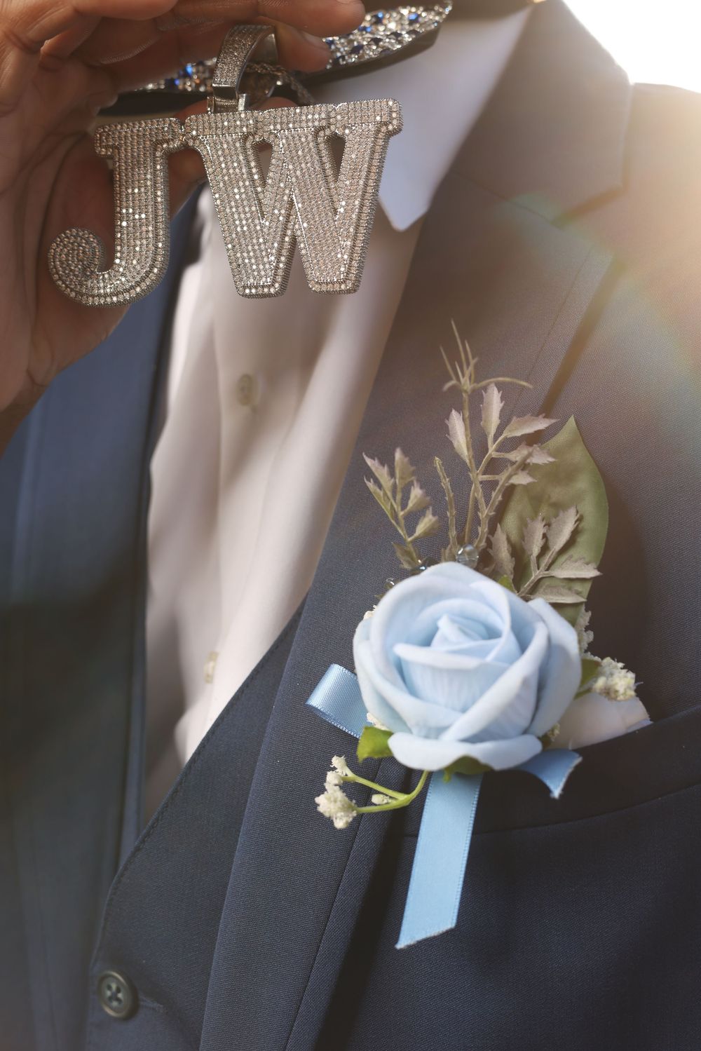 Close-up of navy suit boutonniere with blue rose and rhinestone JW initials jewelry accessory.