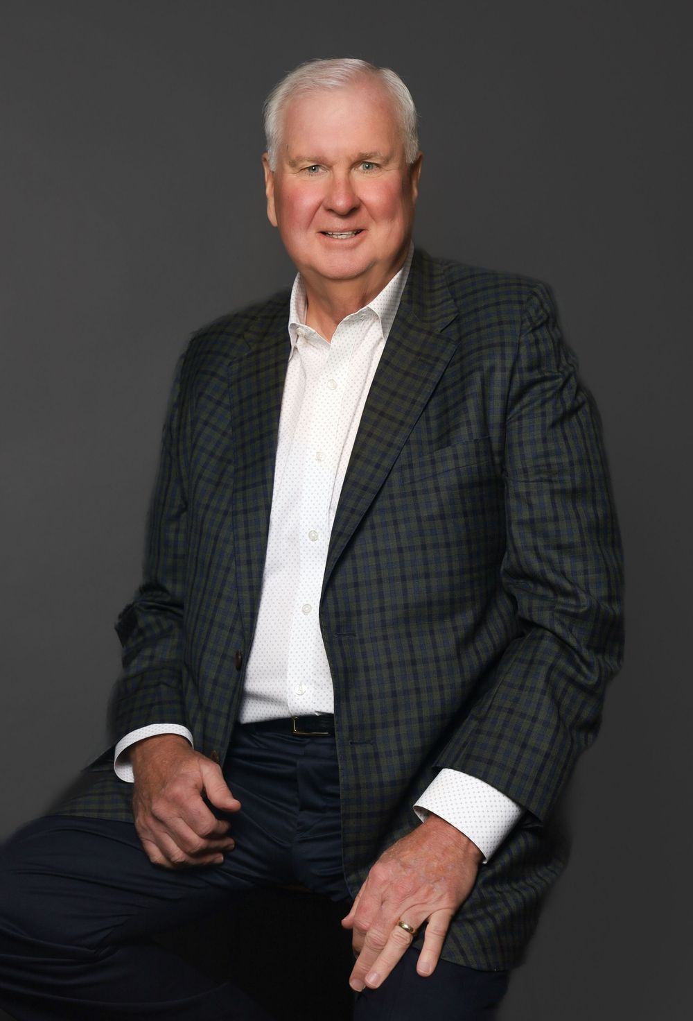 Professional senior man in plaid blazer poses confidently for corporate headshot on gray background.