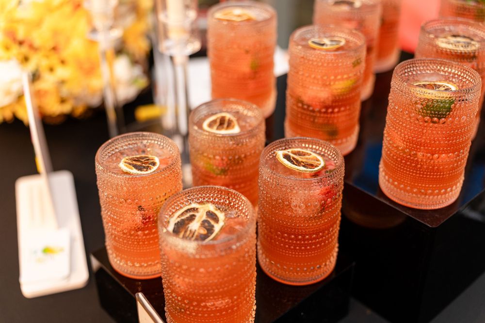 Several pink or coral-colored cocktails in glass tumblers with ornate designs arranged on a dark surface.