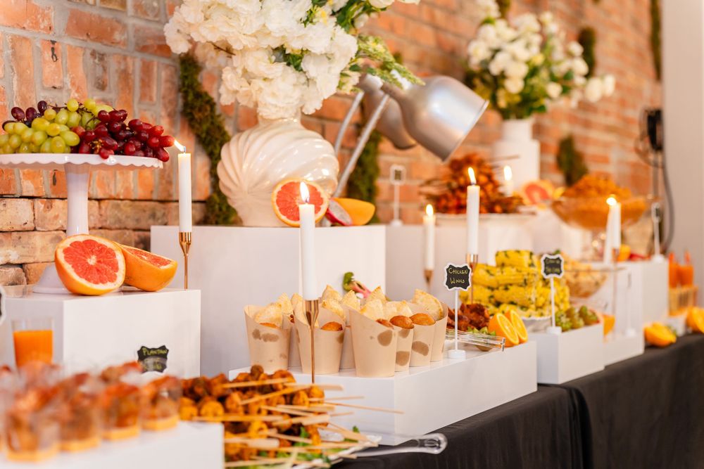 Elegant dessert table with citrus fruits, candles and floral arrangements set against rustic brick wall backdrop.