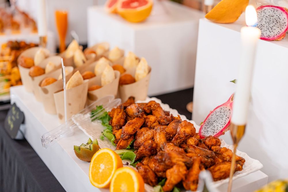 Catering display of crispy fried chicken wings with orange slices and appetizers served on white platters.