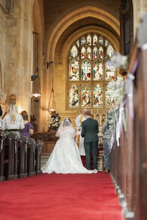 Wedding ceremony in traditional church with stunning stained glass window and red carpet aisle.