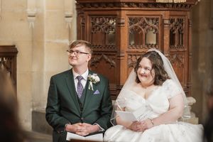 Newlyweds seated together in a church with ornate wooden carvings and architecture.