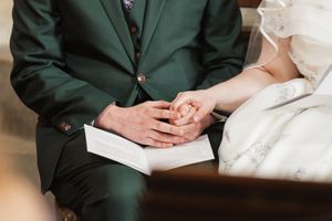 Couple holding hands over a Bible during a wedding ceremony, with the groom wearing a dark green suit.