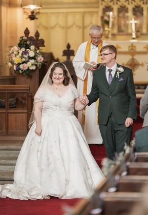 Wedding ceremony in traditional church with bride in white dress and groom in green suit.