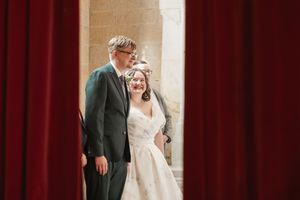 Intimate moment shared between wedding couple against red curtain backdrop in church setting.
