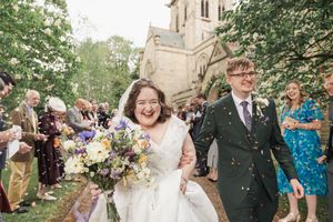 Newlyweds walk through shower of confetti outside church with joyful expressions.