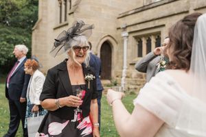Wedding guest in elegant hat shares cheerful moment with others during outdoor reception.