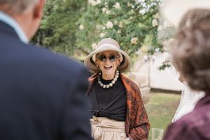 Wedding guest in sunhat and decorative shawl smiles during outdoor reception.