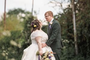 Romantic outdoor wedding portrait with couple in formal attire and floral bouquet.