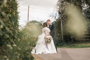 Romantic countryside wedding portrait through green foliage along rustic path.