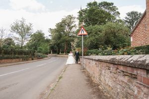 A wedding couple walking along a countryside road with stone walls and trees.
