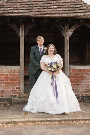 A joyful wedding portrait under a wooden shelter with brick walls.