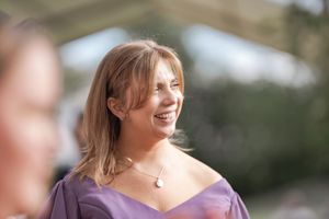 Guest in purple dress smiles during outdoor wedding celebration.