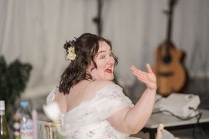 Bride makes expressive gesture during wedding reception with guitar visible in background.
