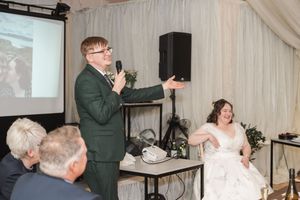Wedding speeches and presentations during reception with projection screen in background.