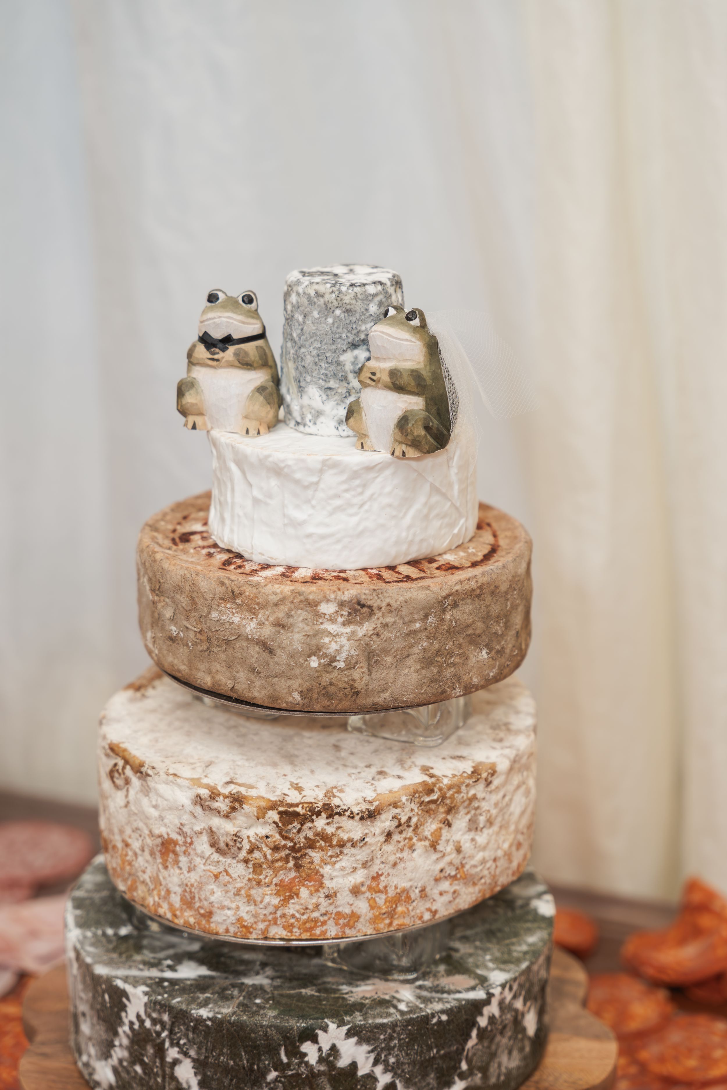 A rustic wedding cake decorated with small frog figurines on top of multiple tiers with textured frosting.
