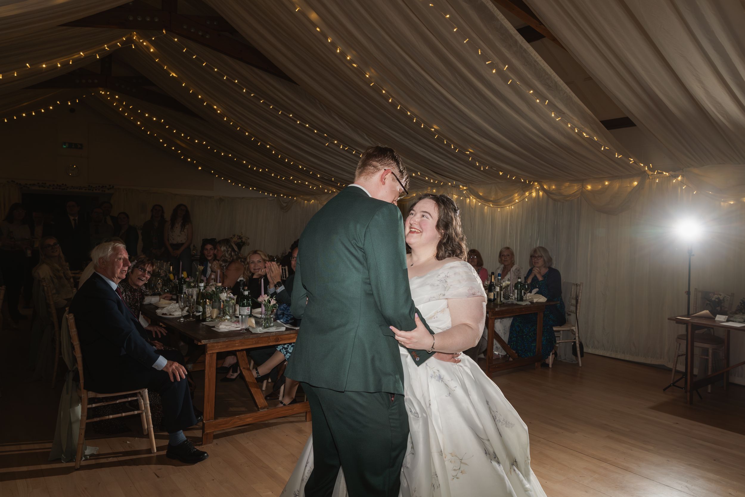 A couple dancing in a reception venue decorated with twinkling fairy lights strung across the ceiling.