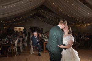 Wedding couple shares an intimate dance under romantic string lights in a reception venue.