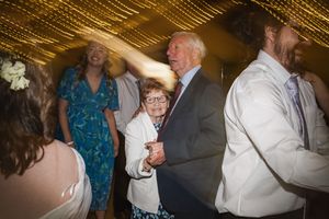 Guests dance and celebrate at a wedding reception under warm golden lighting and decorative ceiling treatments.