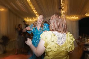 Two guests dancing energetically at a wedding reception under glowing string lights.